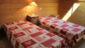 Una habitación acogedora con dos camas, cada una cubierta con un edredón rojo y blanco, una mesita de noche de madera con una lámpara, y un techo inclinado con un tragaluz.