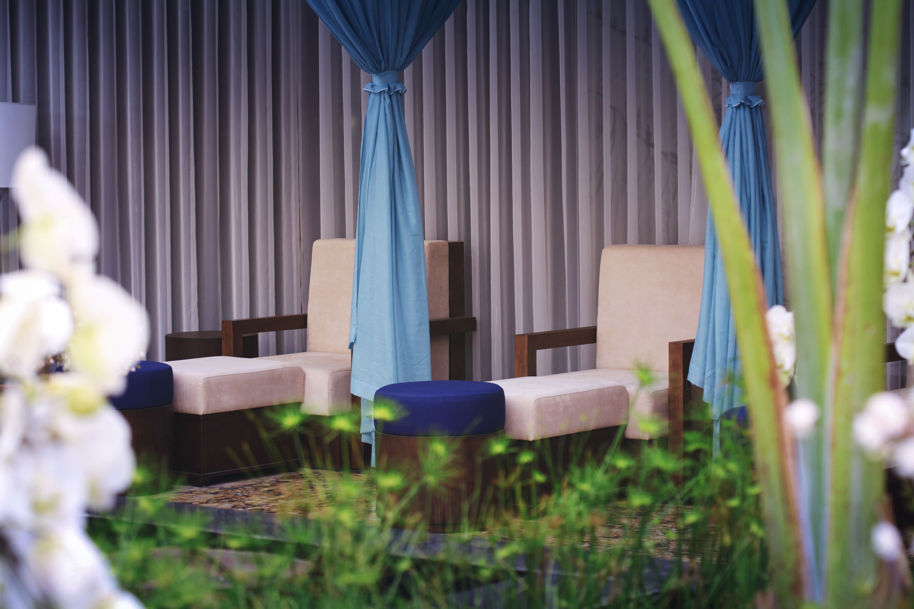 Une pièce avec deux fauteuils beiges, un pouf bleu et un rideau en arrière-plan.