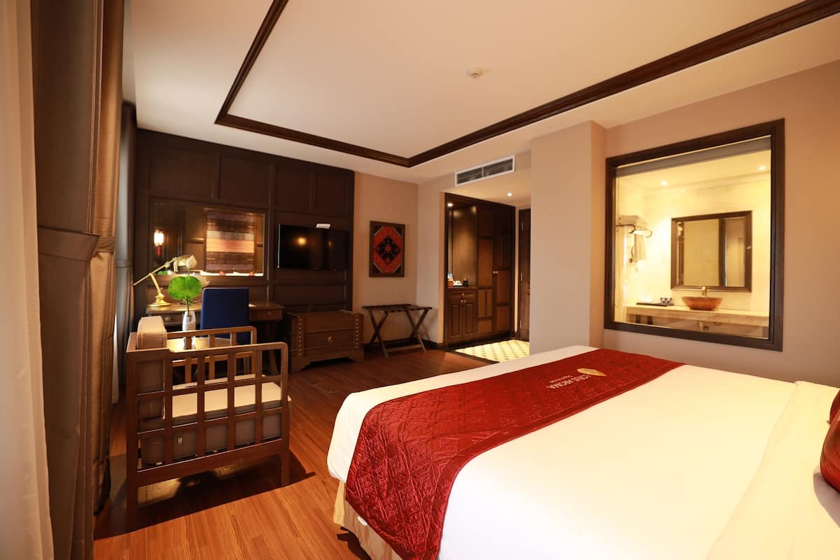 Habitación de hotel con una cama grande, un escritorio, una silla, una mesita, un espejo y una puerta que da a un baño.