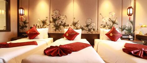 Habitación de hotel con tres camas, cada una con almohada y manta rojas.
