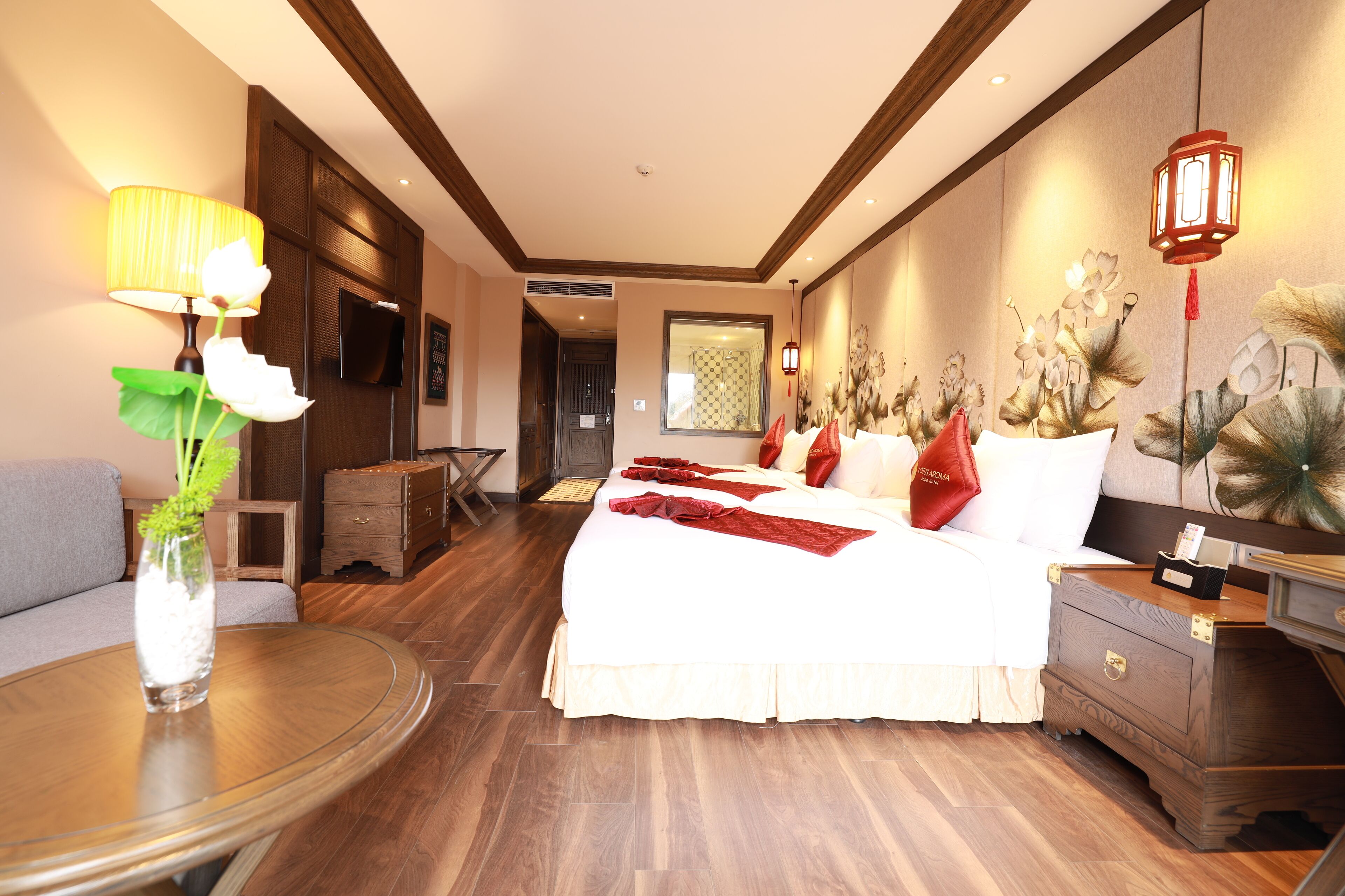 Een hotelkamer met een groot bed, een houten nachtkastje, een ronde tafel met een vaas, en een aan de muur bevestigde televisie.