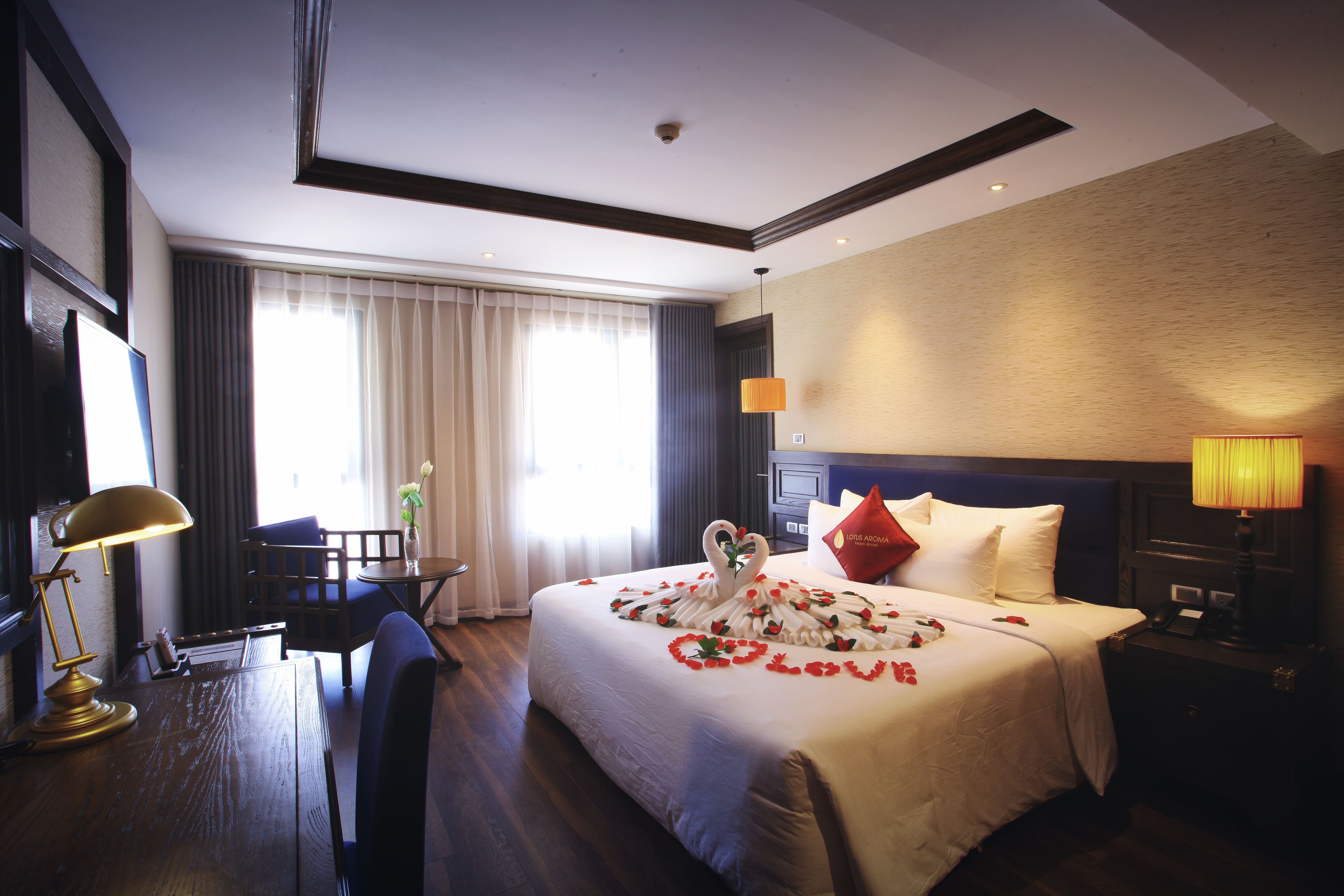 A hotel room with a large bed, a desk with a lamp, a chair, and a nightstand with a lamp.