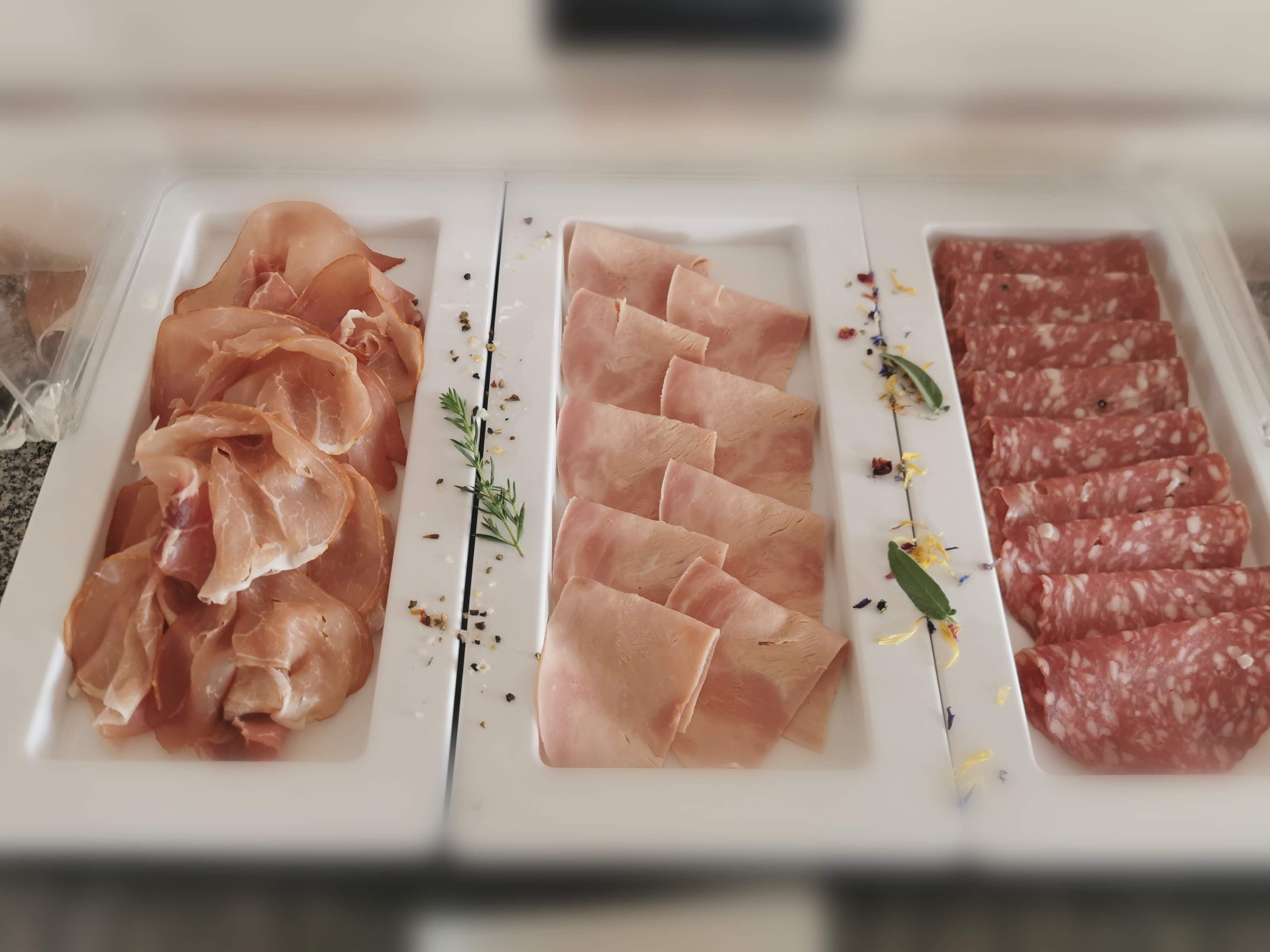 A display of various cured meats on a white tray with decorative herbs.