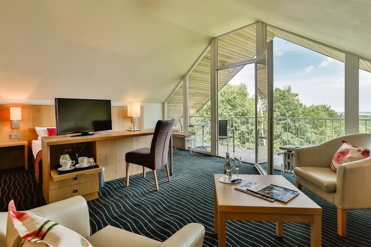 A hotel room with a large window, a television, a desk, a chair, a sofa, and a coffee table.