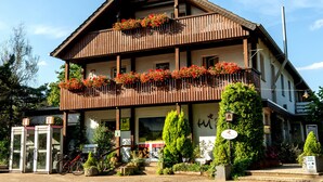 A two-story building with a balcony adorned with flowers, a sign indicating a restaurant, and a bicycle parked outside. - Berghotel Hohe Mark (Reken)