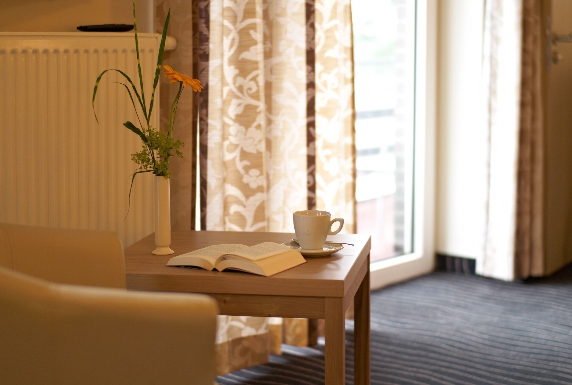 A hotel room with a wooden table, a white cup, and an open book.