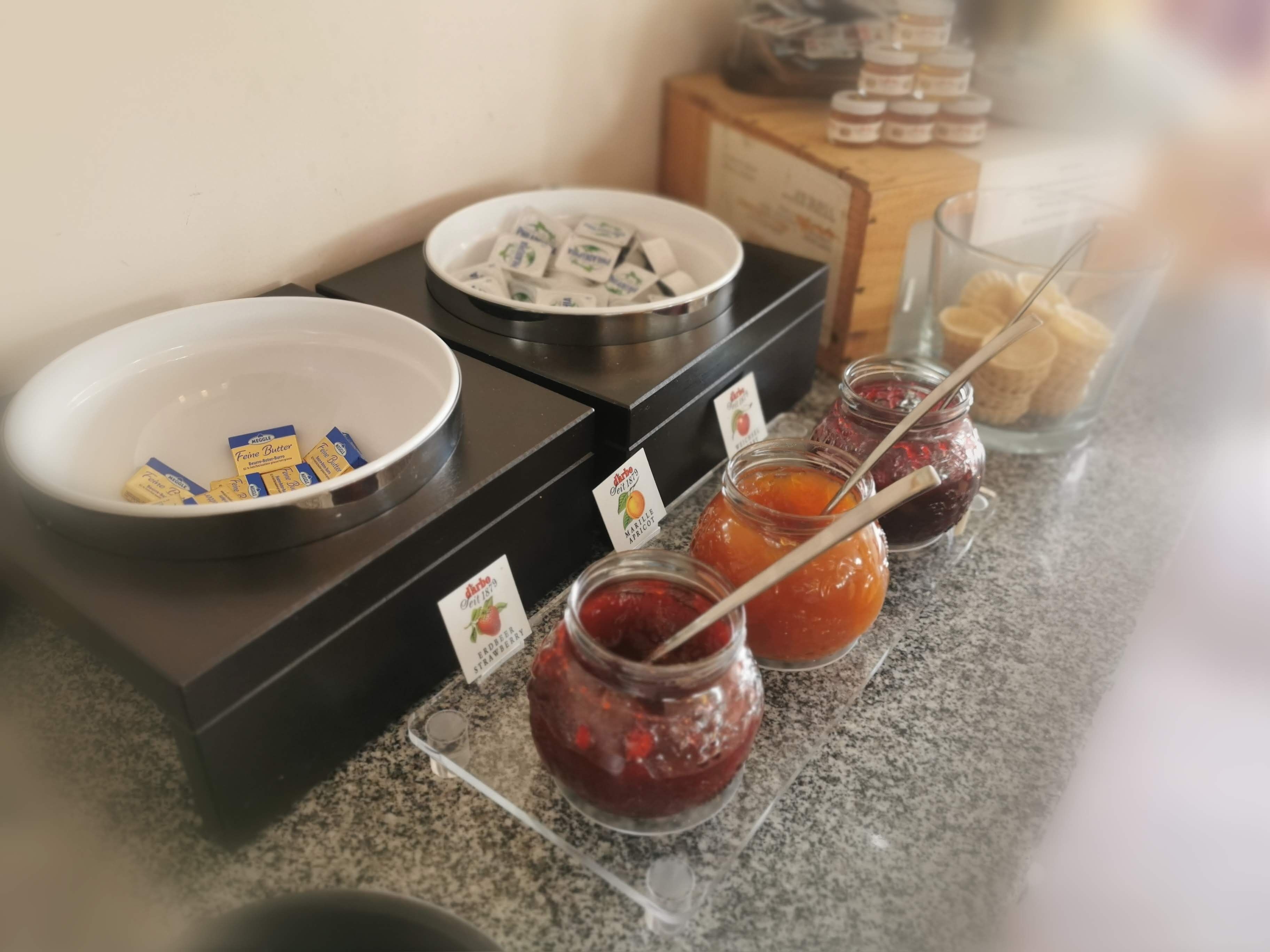 A buffet setup with a bowl of butter, a plate of cheese, and jars of jam.
