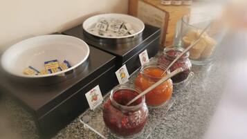 A buffet setup with a bowl of butter, a plate of cheese, and jars of jam.