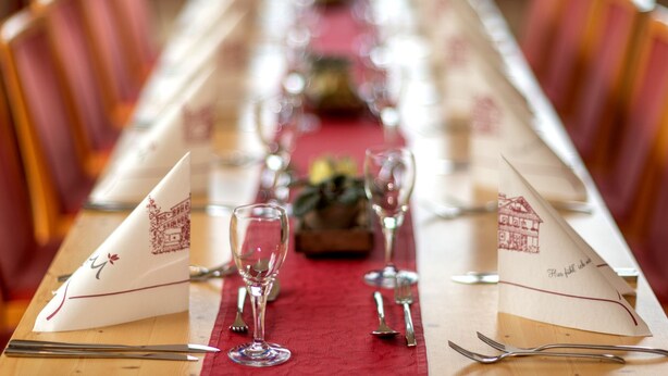 A long dining table set with red tablecloth, white napkins, and silverware. - Berghotel Hohe Mark (Reken)