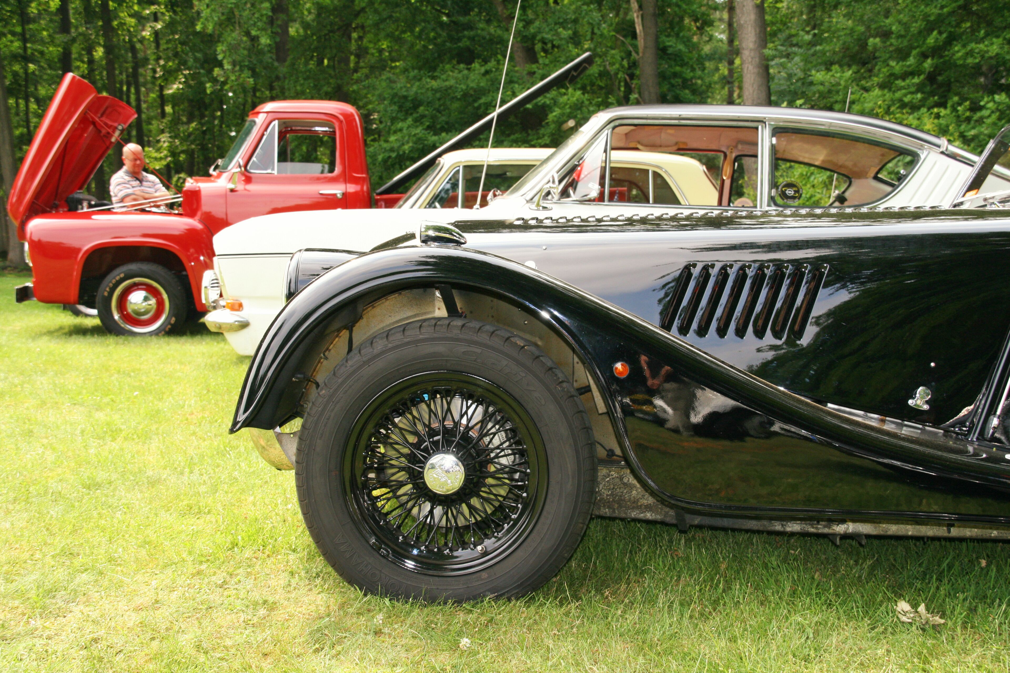 A vintage car with a hood open, parked on grass.