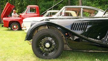 A vintage car with a hood open, parked on grass.