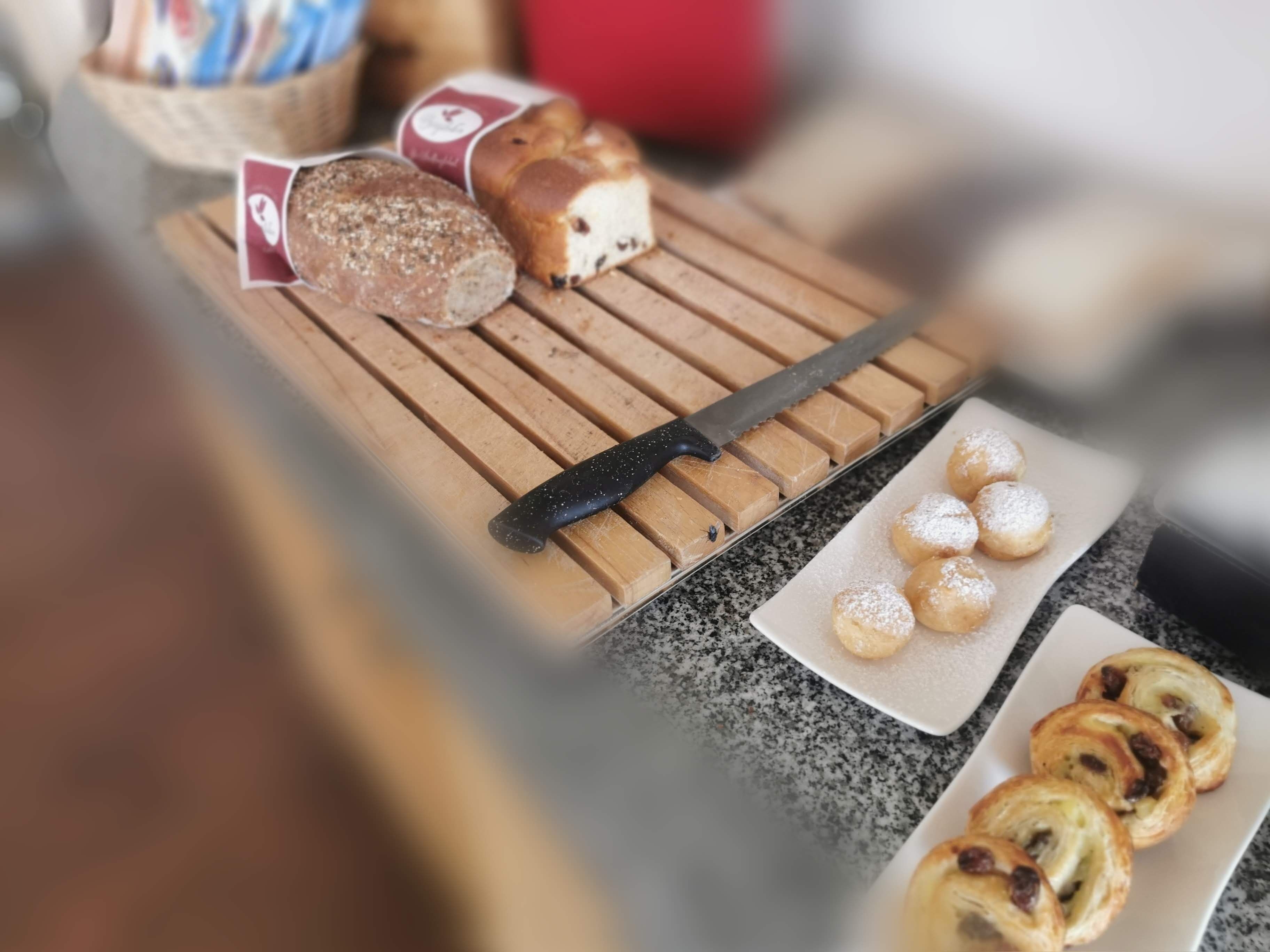 Tábua de madeira com pão fatiado, uma faca e doces sobre um balcão de granito.