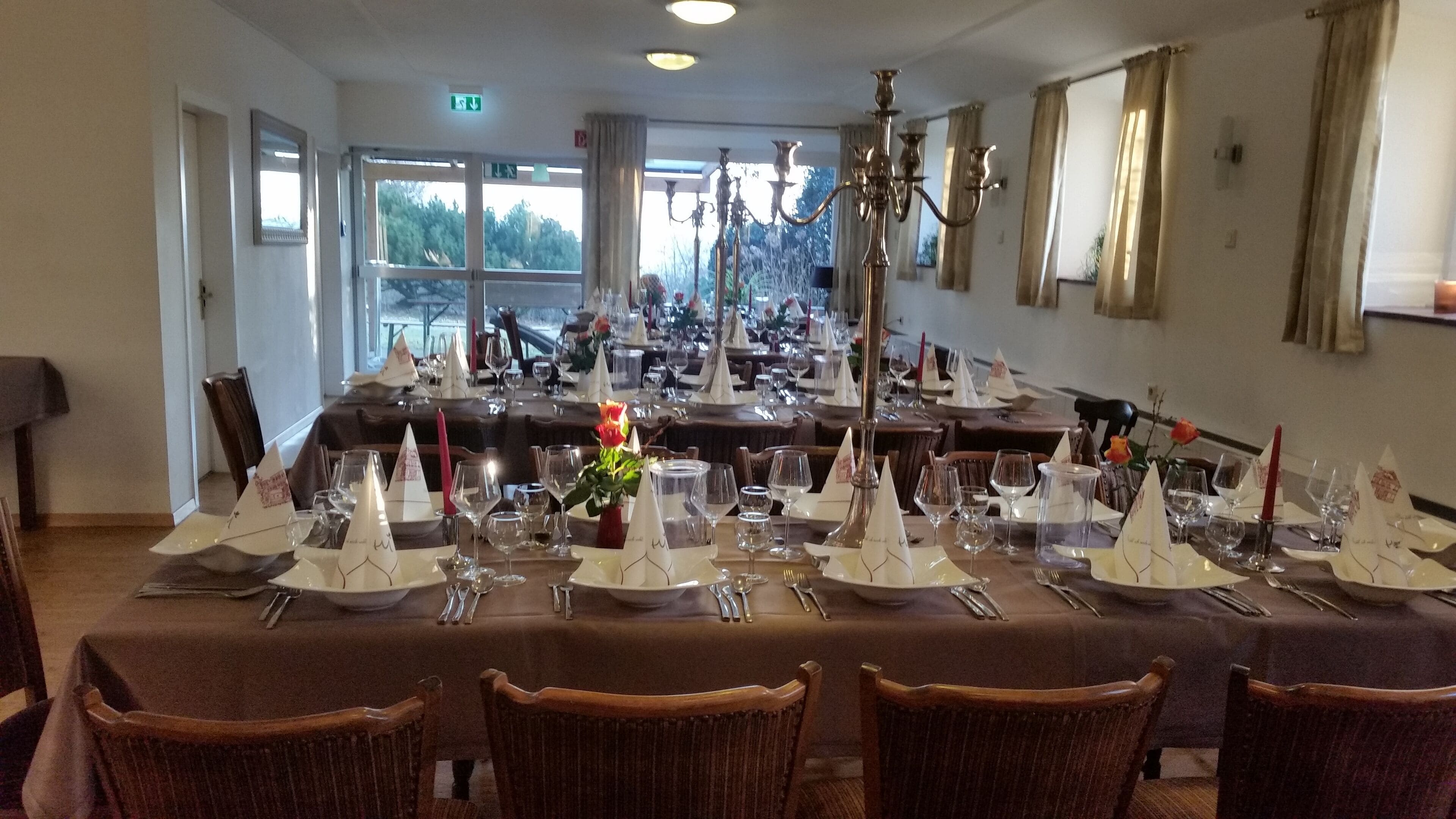 Un comedor con varias mesas dispuestas para una comida, con manteles blancos, cubertería ordenada y candelabros.