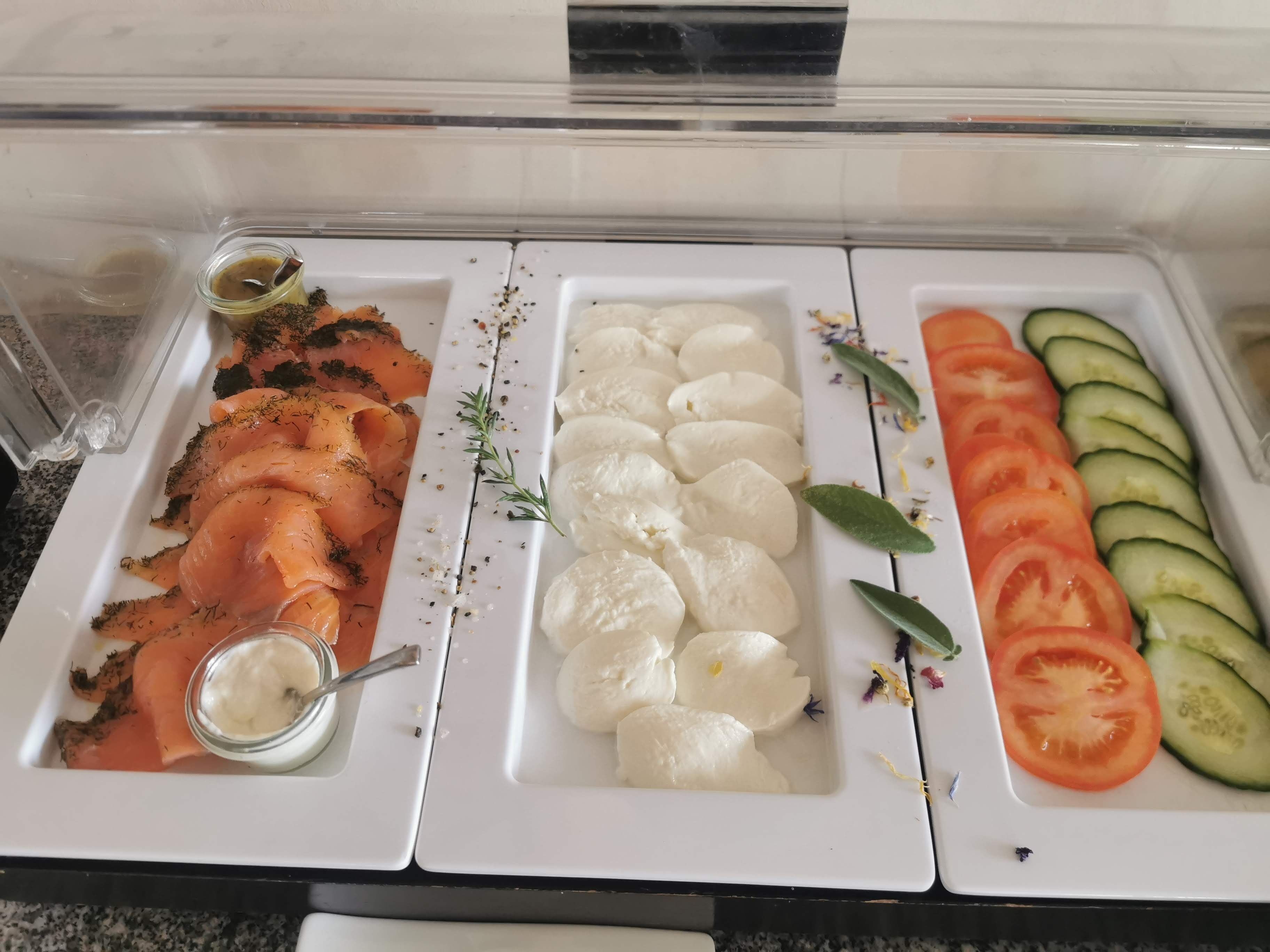 A buffet with smoked salmon, mozzarella cheese, and sliced tomatoes and cucumbers.