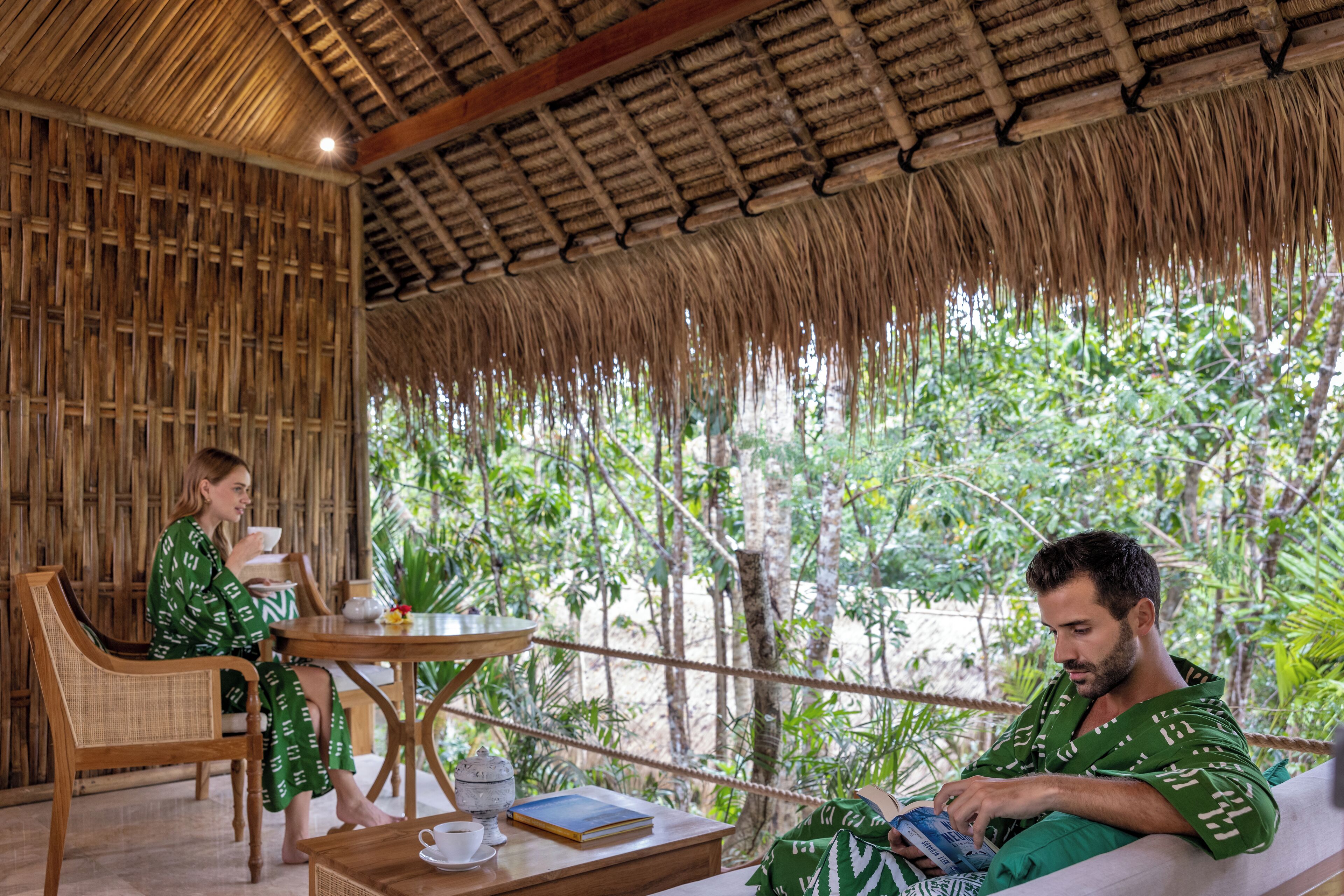 A room with a thatched roof, wicker furniture, and a view of lush greenery.