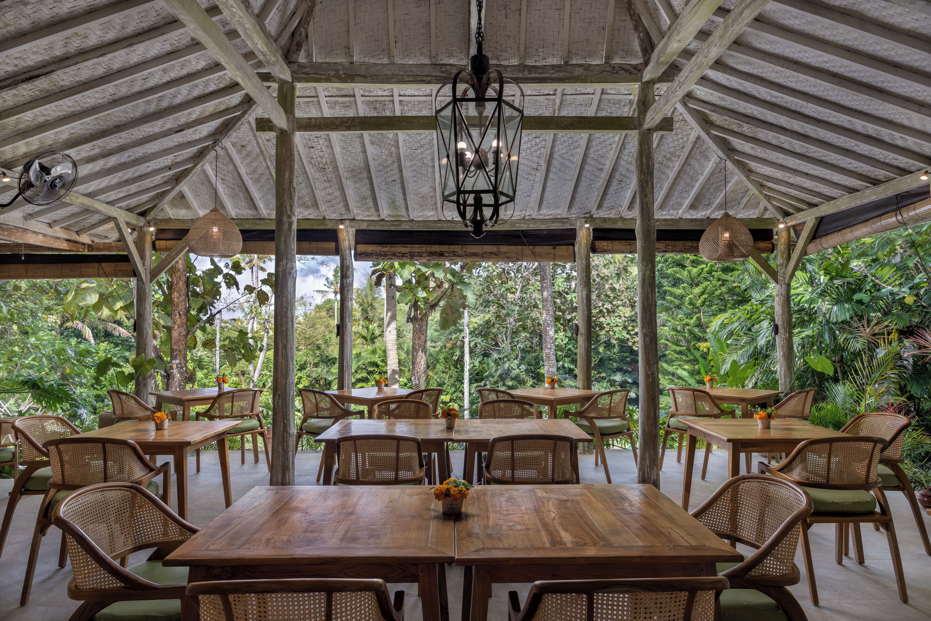 An outdoor wooden pavilion with tables and chairs, surrounded by lush greenery.