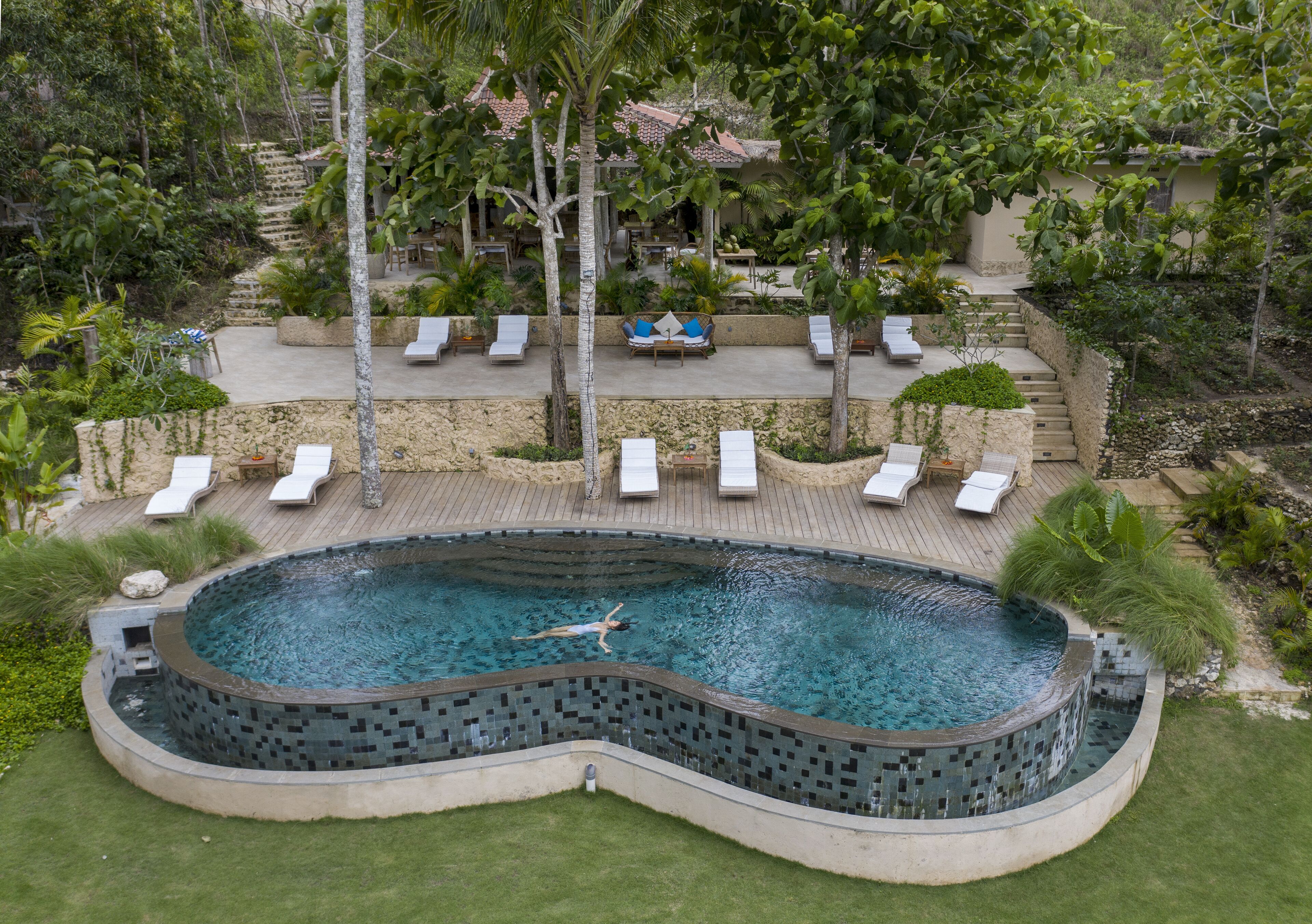 A swimming pool with a tiled edge, surrounded by lounge chairs and a stone wall.