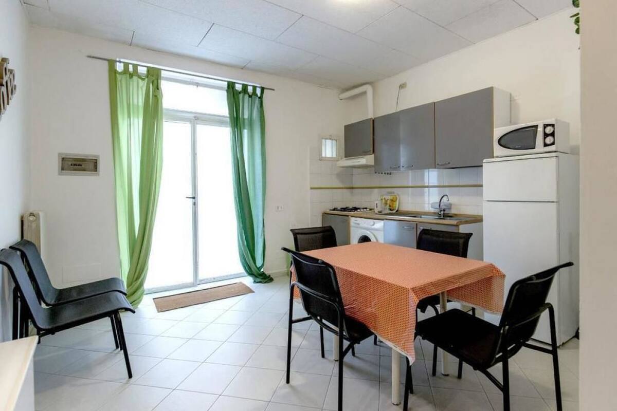 A small kitchen with a microwave, stove, and sink. There is a dining table with four chairs.