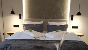 A modern bedroom with a large bed, two bedside tables, a wooden bench, and a wall-mounted light fixture. - Flair Hotel Werbetal (Waldeck)