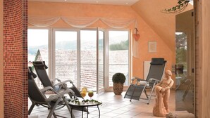 A sunlit room with two reclining chairs, a small table with drinks, and a statue. - Flair Hotel Werbetal (Waldeck)