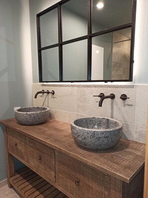 Un baño con dos lavamanos de granito, un mueble de tocador de madera y un espejo grande sobre los lavamanos.