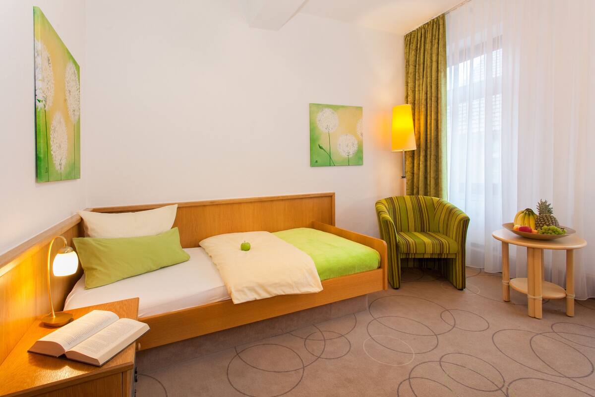Une chambre d’hôtel avec un lit, une chaise, une petite table avec des fruits et une lampe.