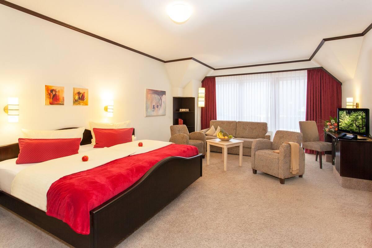 Une chambre d’hôtel comprenant un lit, deux fauteuils, un canapé, une petite table et un téléviseur.