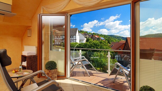 A balcony with a view of houses and trees, a chair, a small table with a bottle and apples, and a potted plant. - Flair Hotel Werbetal (Waldeck)
