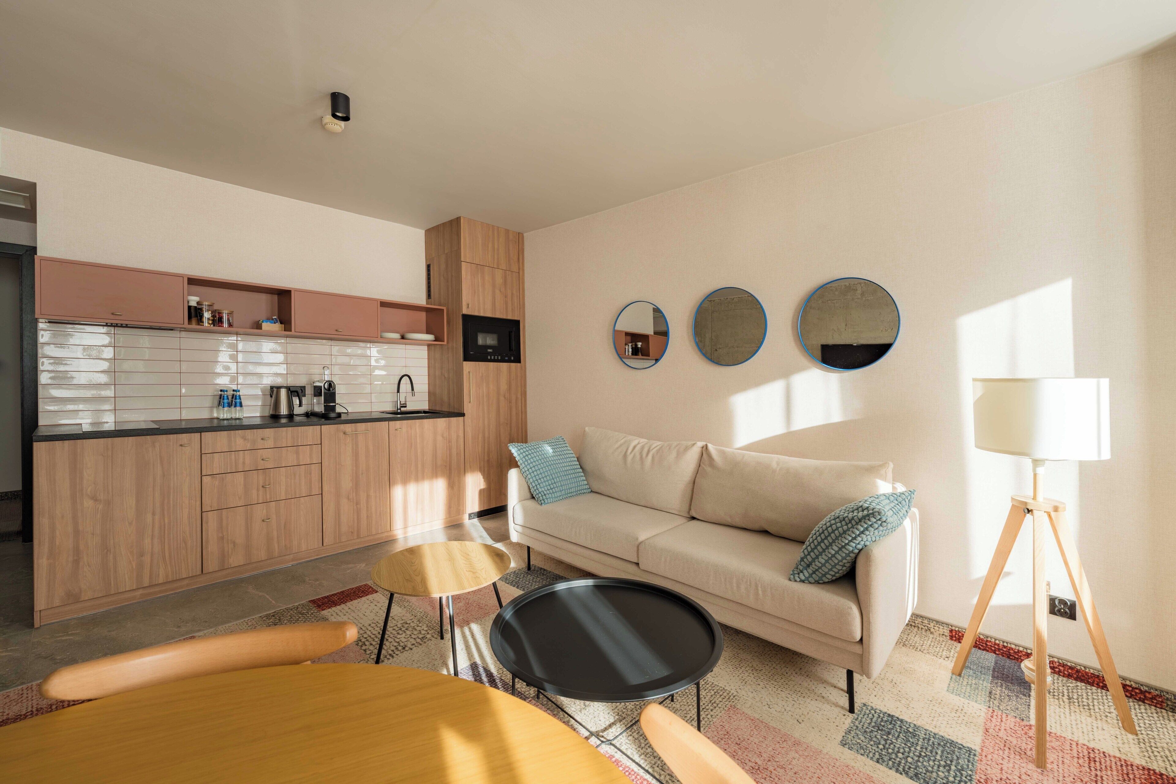 A modern living space with a kitchen, a sofa, a dining table, and a lamp.