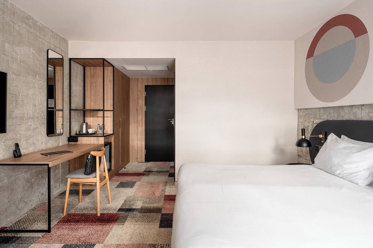 A modern hotel room with a bed, desk, chair, and a large mirror.