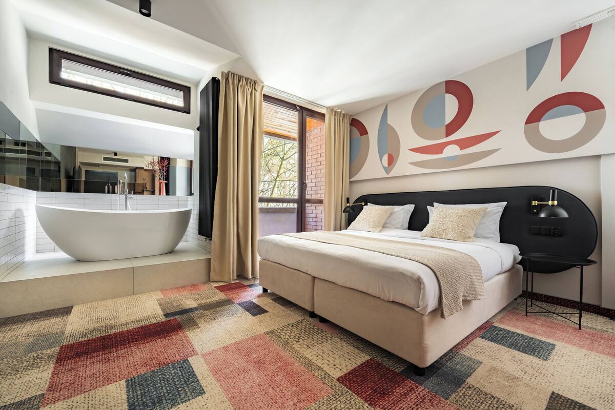 A modern bedroom with a large bed, a built-in bathtub, and a view of the outdoors.
