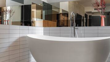 A modern bathroom with a freestanding bathtub, a large mirror, and a vase with red berries.