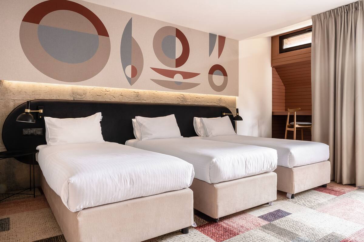 A hotel room with two beds, a large abstract wall art, a window with curtains, and a small wooden chair.