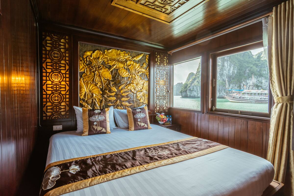 Ein großes Bett mit Blumenmuster am Kopfteil, Holzvertäfelung und Blick auf Boote durch ein Fenster.