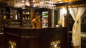 Un espace bar avec un barman, des étagères remplies de bouteilles et de verres, et une fenêtre décorative offrant une vue agréable.