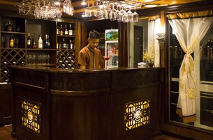 Zona de bar con un cantinero, estantes llenos de botellas, vasos y una vista decorativa por la ventana.