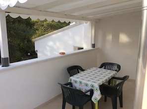 Un balcón con mesa y sillas, un muro blanco y vistas al verdor.