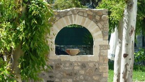 Estructura de piedra con una ventana circular y un cuenco en su interior, rodeada de follaje.