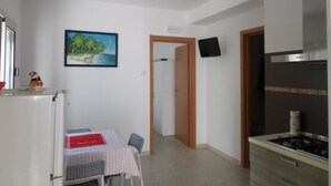 Una cocina compacta con refrigerador, una mesa de comedor con sillas, un cuadro en la pared y un televisor sobre una puerta.