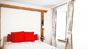 A bedroom with a bed, red pillows, a wooden headboard, a radiator, and curtains.