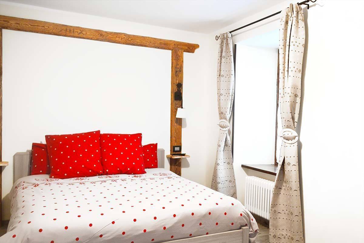 Une chambre à coucher avec un lit, des oreillers rouges, une tête de lit en bois, un radiateur et des rideaux.