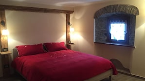A bedroom with a bed, two bedside tables, a stone window, and a wooden beam ceiling.