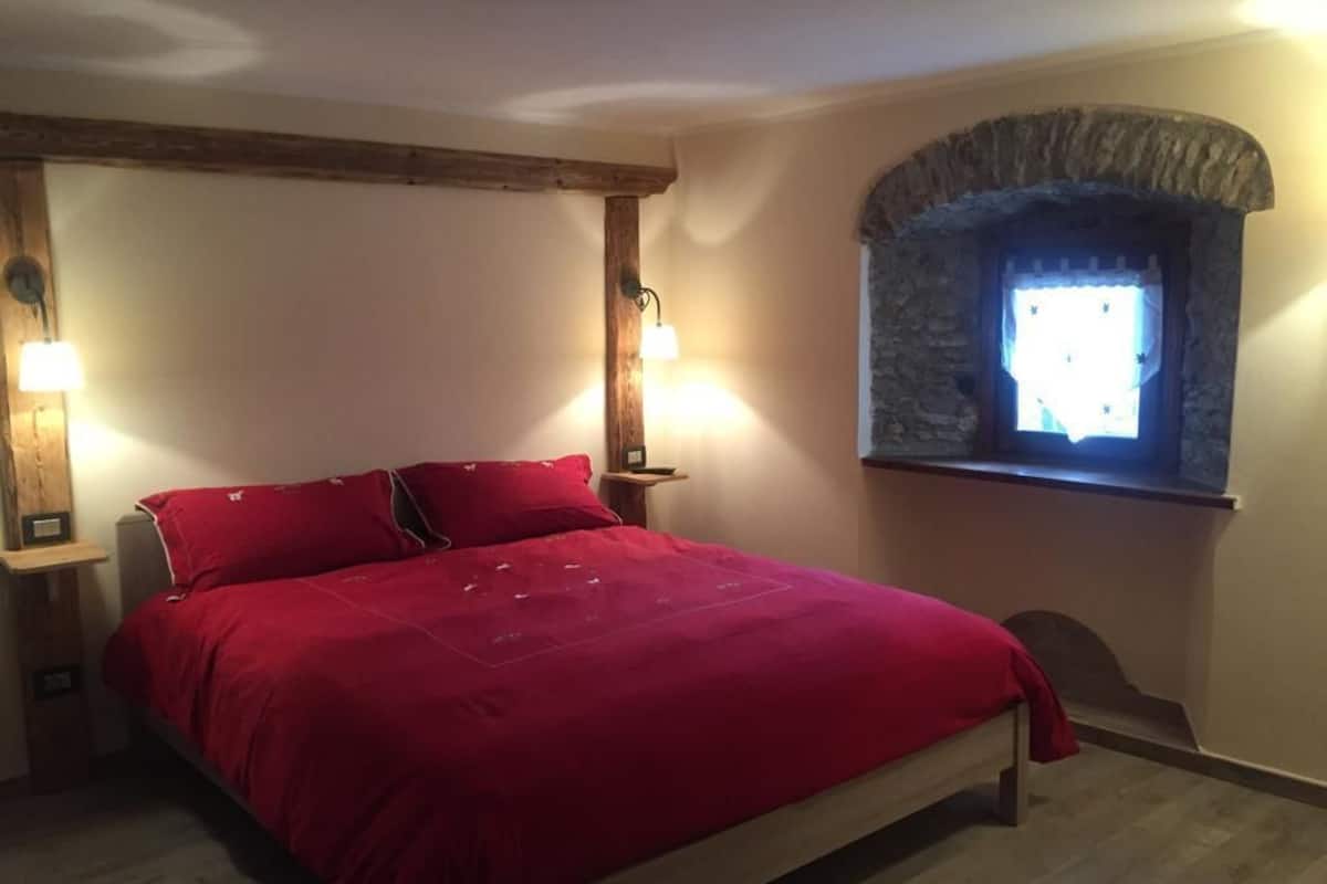 Une chambre à coucher avec un lit, deux tables de chevet, une fenêtre en pierre et un plafond avec une poutre en bois.