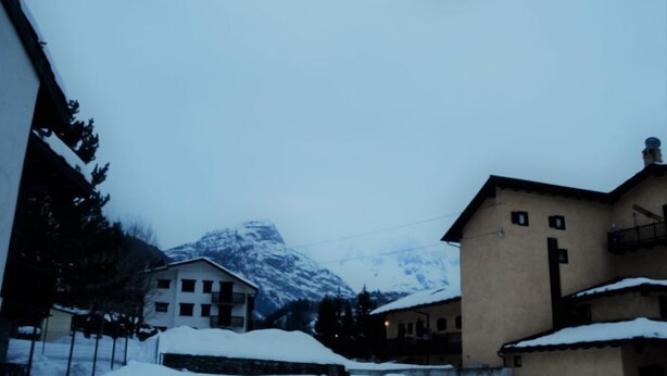 A snow-covered mountain village with traditional buildings and a prominent mountain in the background.