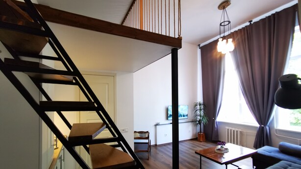 Ett modernt vardagsrum med en trätrappa, en soffa, ett soffbord och en krukväxt.