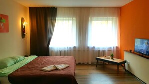 Ett hotellrum med en säng, ett litet bord med en växt, en tv och ett fönster med gardiner.