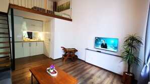 Ett modernt vardagsrum med trägolv, ett matbord med en mittdekoration, en tv som är monterad på väggen och en trappa som leder upp till en övre våning.