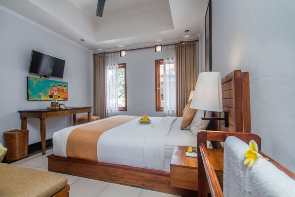 A hotel room with a large bed, a desk, a television, and a painting on the wall. - Hartaning House by GenuineHost (Ubud)