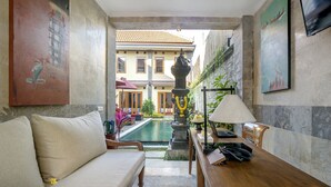 Habitación de hotel con sofá, una mesita con lámpara, una estatua y vistas a una piscina y un edificio al fondo.