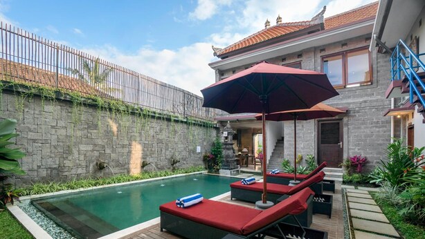 Piscina con sillones de descanso y una sombrilla, rodeada de un muro de piedra y follaje.